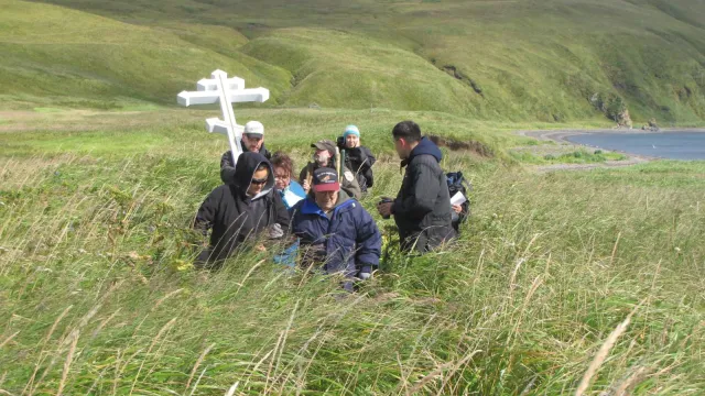 Group of people around a Russian cross in tall grass