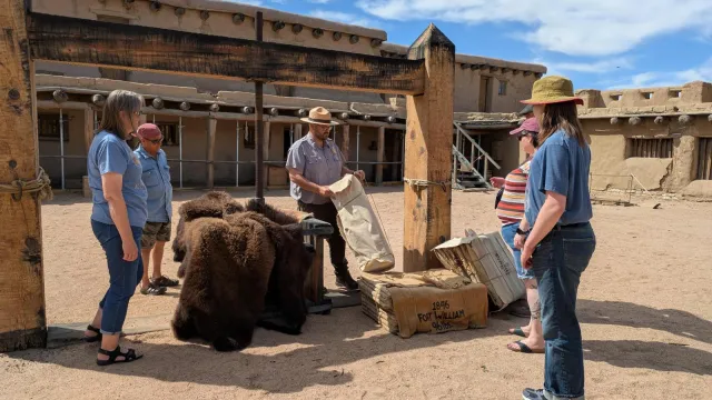 A group of visitors stand around a large wooden apparatus in a plaza courtyard.