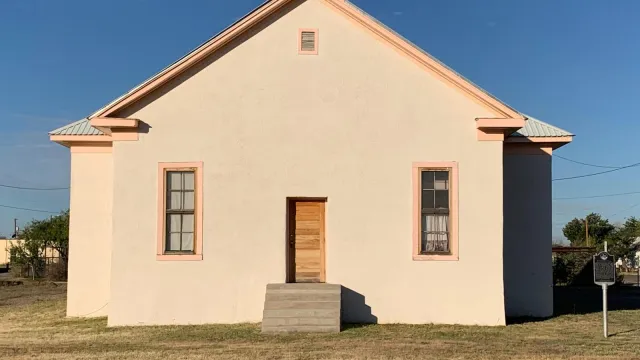 cream colored building with two windows and a wooden doorway with steps leading up to it.