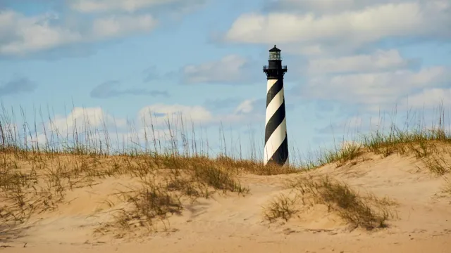 A beach landscape with the black and white spiraled lighthouse in the background