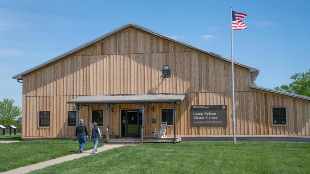 A paved path leads to a gray wooden building with US Flag flying.
