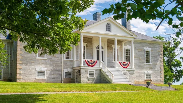 American flag bunting hangs from the porch on a limestone building with a white portico.