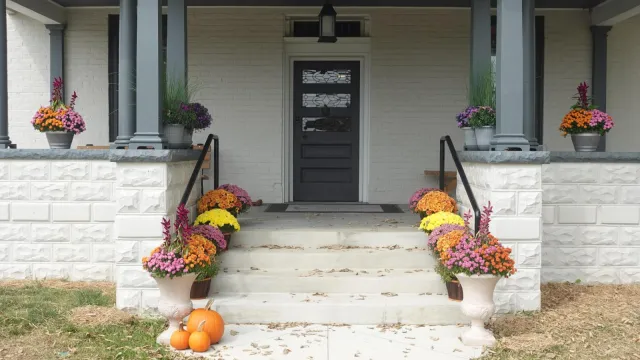 A large grey house with dark grey shutters with a green lawn out front under a blue sky