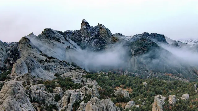 Snow dusted granite formations jut up from a mountainous juniper covered landscape.