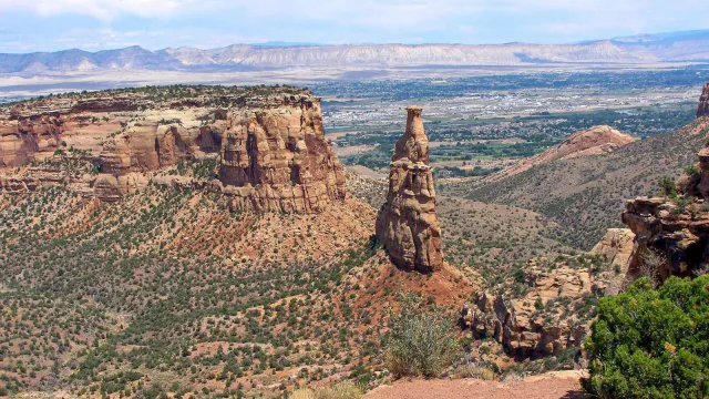 sandstone spire hundreds of feet tall stands above sparsely vegetated canyon bottom and cliffs
