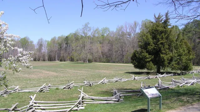 Wooden split rail fencing and flowering trees surround a grassy field behind an interpretive panel