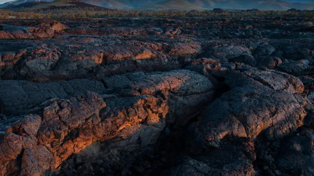 A close-up shot of a folded, waving sea of lava rock, with mountains in the far distance.