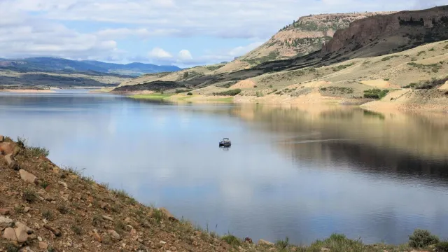 A single boat floating out in a reservoir. Mesas surrounding the area are reflected on the water.