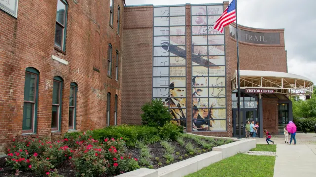 A three-story brick building with tall green windows and a tall photo mural on the glass wall
