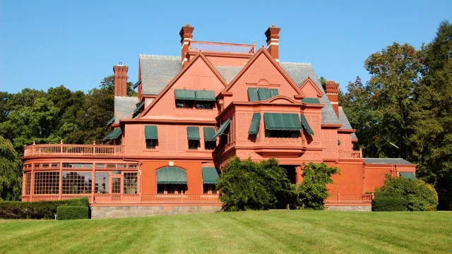 Large salmon colored Victorian mansion with green lawn and blue sky