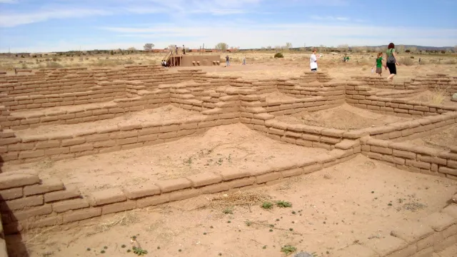 tan-colored pueblo Indian ruins with blue sky and three people