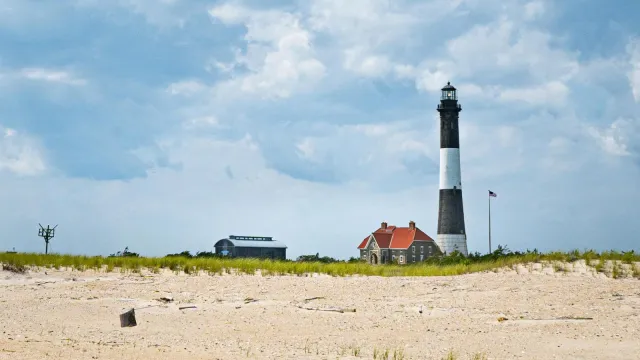A wide shot of the white and black striped Fire Island Lighthouse from the beach.
