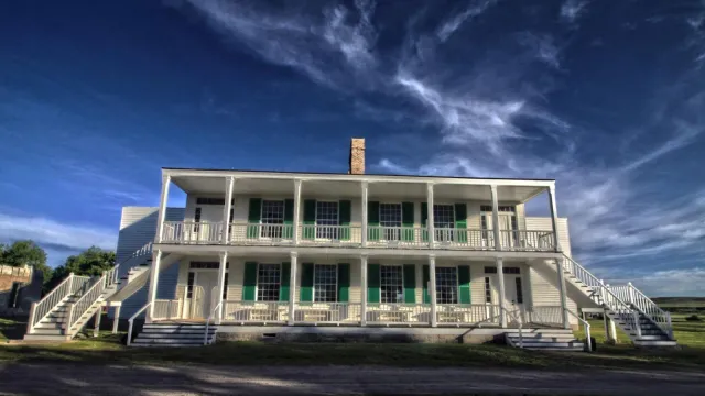 A large two story white building with pillars. Several windows with green shutters