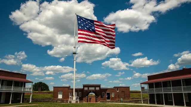 A large American flag waved over the brick sallyport of an old fort.