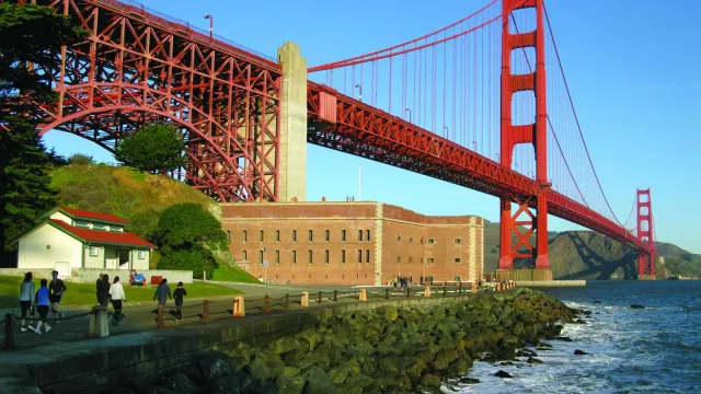 Fort Point with visitors approaching on road in front and Golden Gate Bridge above.