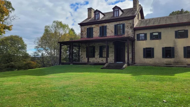 front view of historical Stone House and Visitor Center with green grass lawn with trees and clouds