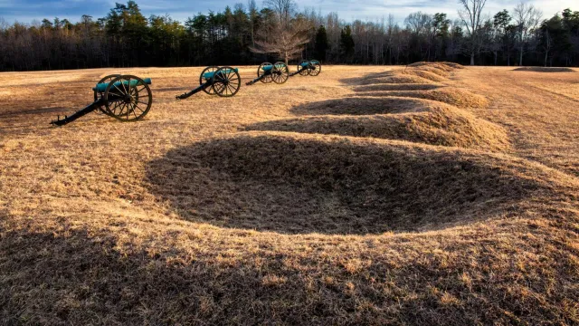A line of four cannons placed in front of crescent shaped earthen gun pits.