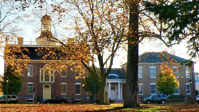 Red, yellow, and green leaves lay on the grass in front of a colonial building.