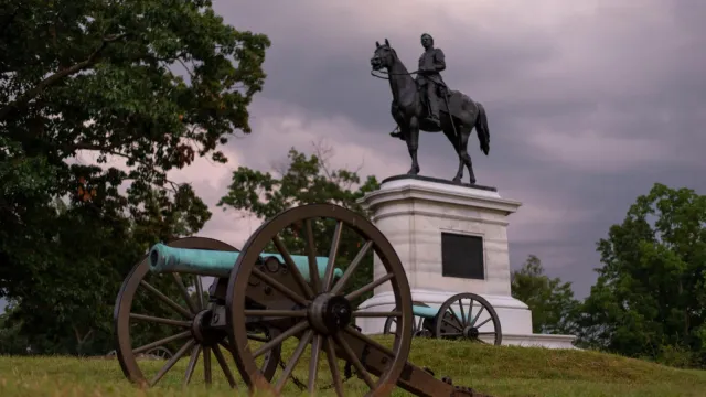 A canon sits in front of an equestrian statue.
