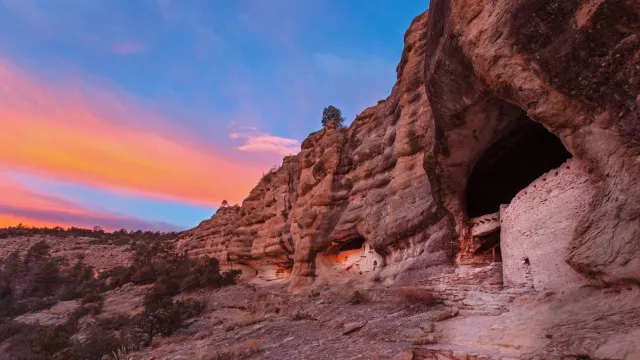 Sunrise view of Gila Cliff Dwellings with brilliant sky.