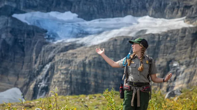 A park ranger standing with arms out in front of snow and ice.