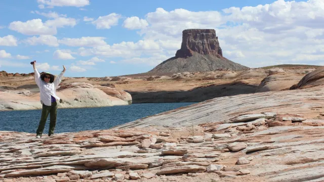 Woman raises her arms while standing in front of a sandstone butte
