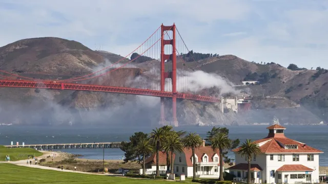 White buildings with red roofs at Crissy Field with blue bay and Golden Gate Bridge and fog behind.
