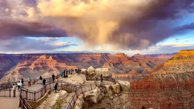 At Sunset, swirling rain clouds above a vast canyon filled with colorful peaks and cliff walls.