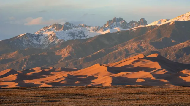 Grasslands, large dunes, and snow-capped peaks at sunset