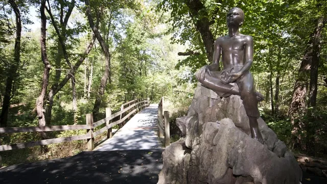 Bronze status of young George Washington Carver atop a large boulder, on the Carver trail.