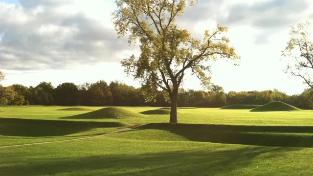 An early morning sun casting long shadows over grass-covered mounds.