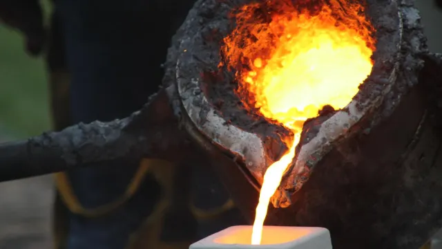 Melted iron pouring into a mold from a metal bucket.