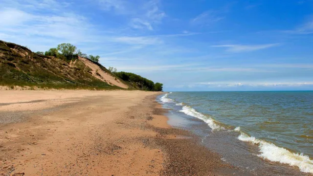 Michigan Lake beach with green grassy dunes in the background, under a blue sky.