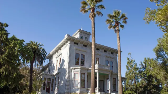 White two story house capped by a bell tower and ringed with palm trees