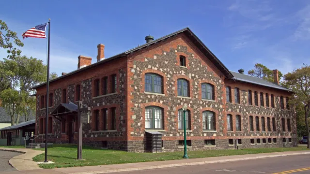 Two story stone and brick building. The American flag flies in front of a blue sky background