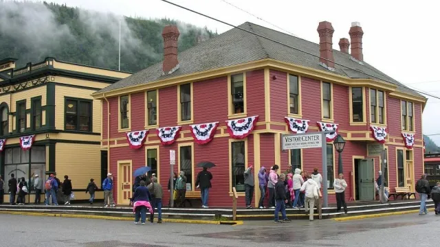 Visitors stand on a boardwalk outside a brick red colored wooden building with tidy golden trim.