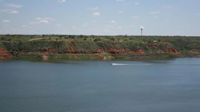 A boat travels across Lake Meredith on a sunny day.  The lake is light blue.