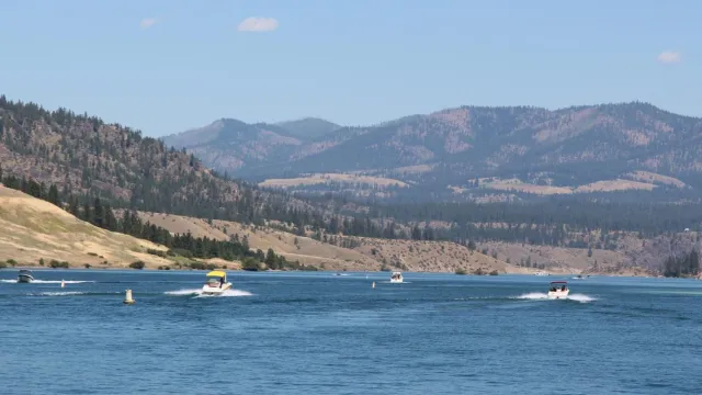 Various motorboats on a blue lake, landscaped by tall tree filled hills.