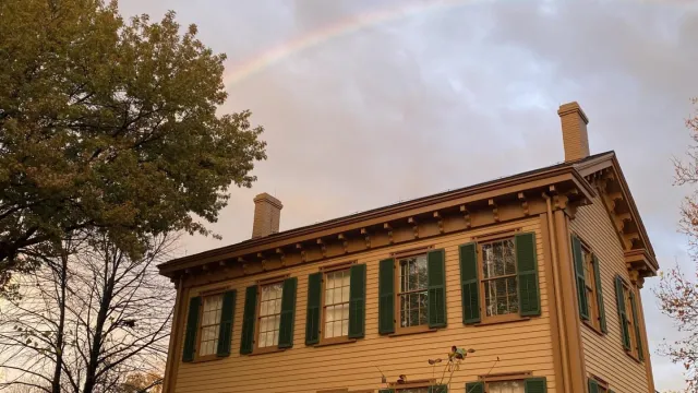 The two-story, tan Lincoln Home with a rainbow in the sky above it.
