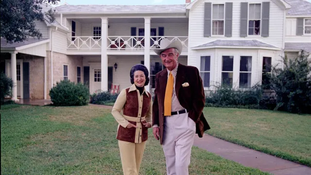 President and Mrs. Johnson stand with their small, white dog in front of the Texas White House.