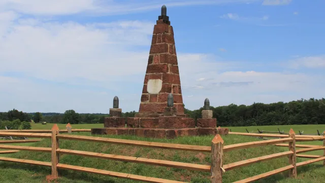 Red sandstone obelisk surrounded by post and rail fence.
