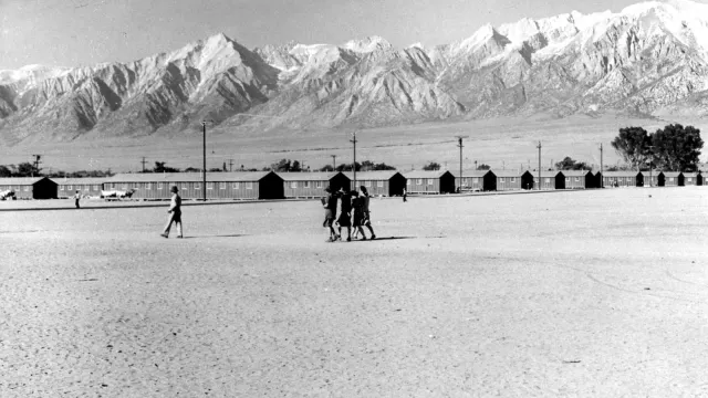People walk to barracks framed by mountain peaks.