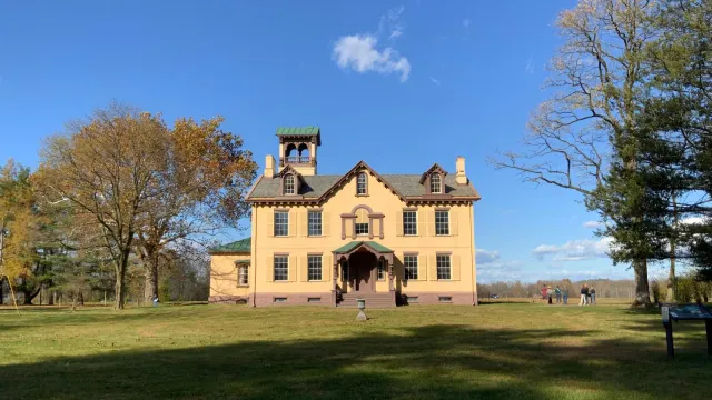 Lindenwald, a yellow, 3 story mansion, is surrounded by trees.