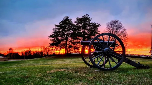 A orange sunset over the white granite headstones in the national cemetery with silhouetted cannon.