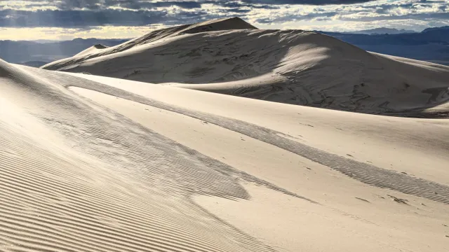 Kelso Dunes with rays of light coming through the clouds. Mountains in the background..