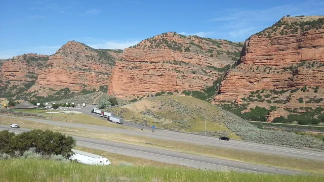 Red cliffs line a highway as seen from a high point with grass in the foreground.