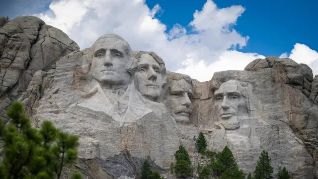 Photo of Mount Rushmore under a bright blue sky with puffy clouds floating over.