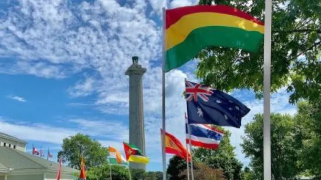 9-3'x5' international flags line sidewalk that leads to a white building with green roof. Tall stone