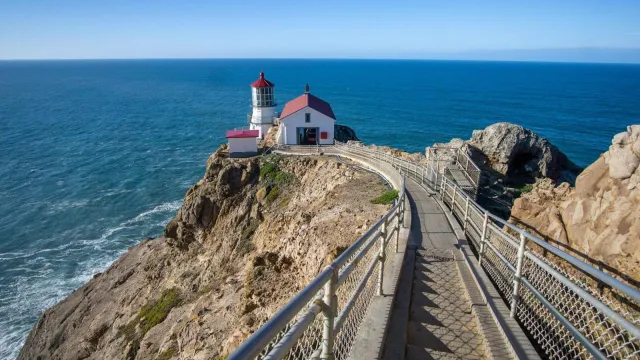 A long concrete staircase down to a red roofed, white lighthouse on cliffs above the ocean.