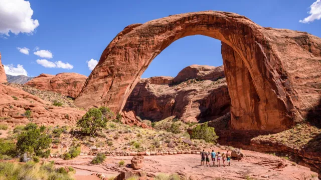 A large natural rock arch spans a canyon with people looking up at it.